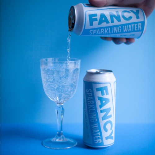 Fancy Sparkling Water being poured into a glass with cans on a blue background